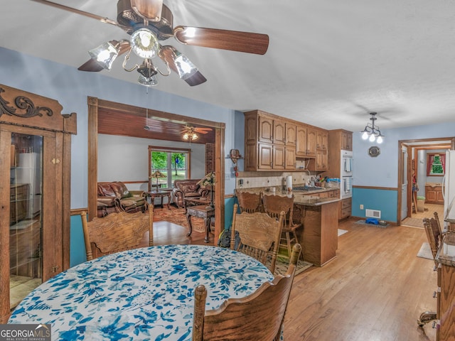 dining room with light hardwood / wood-style flooring and ceiling fan with notable chandelier