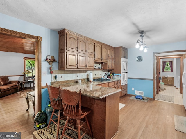 kitchen with stainless steel gas stovetop, a breakfast bar, light stone countertops, a textured ceiling, and light hardwood / wood-style floors