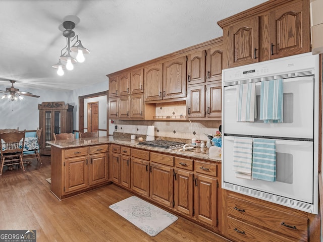 kitchen with ceiling fan, double oven, kitchen peninsula, light hardwood / wood-style floors, and stainless steel gas stovetop