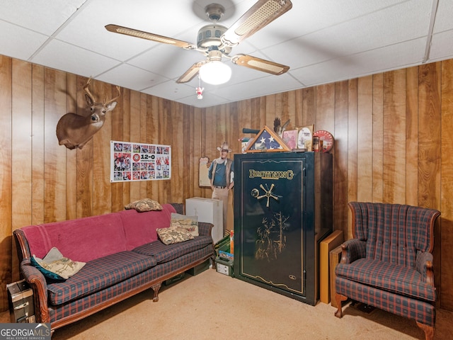 living area featuring a paneled ceiling, wooden walls, carpet, and ceiling fan