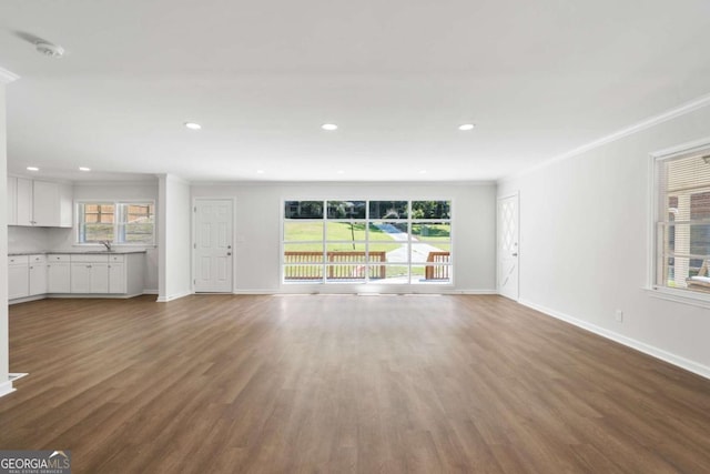 unfurnished living room featuring crown molding, sink, a healthy amount of sunlight, and wood-type flooring