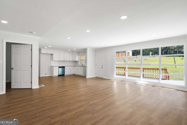 unfurnished living room with sink, dark wood-type flooring, a healthy amount of sunlight, and ornamental molding