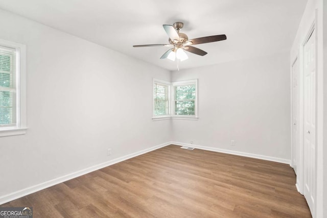 unfurnished bedroom featuring multiple windows, hardwood / wood-style flooring, and ceiling fan