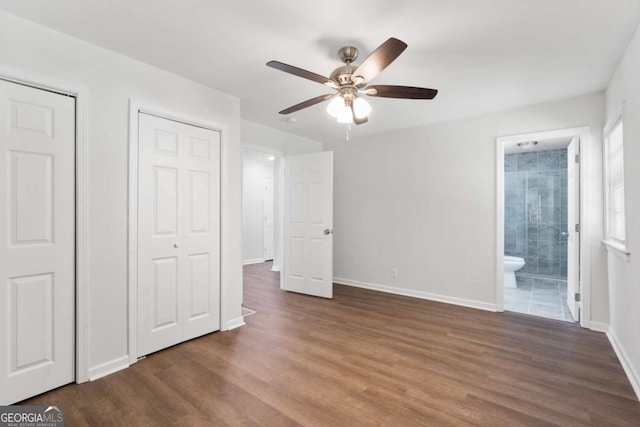 unfurnished bedroom with ensuite bathroom, ceiling fan, dark hardwood / wood-style flooring, and multiple closets