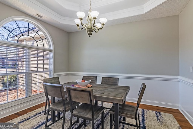 dining space with ornamental molding, hardwood / wood-style flooring, a raised ceiling, and a notable chandelier