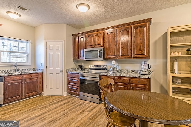 kitchen with light stone countertops, a textured ceiling, stainless steel appliances, sink, and light hardwood / wood-style flooring