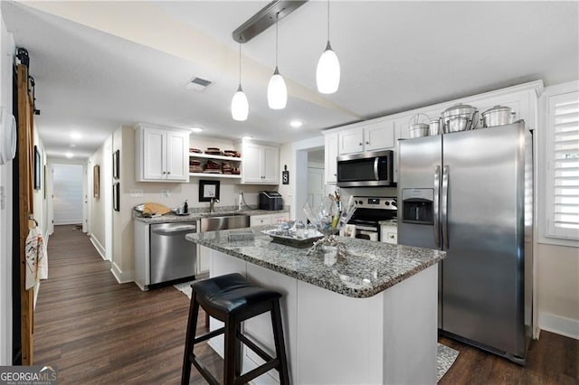 kitchen featuring appliances with stainless steel finishes, dark wood-type flooring, white cabinetry, a kitchen island, and hanging light fixtures