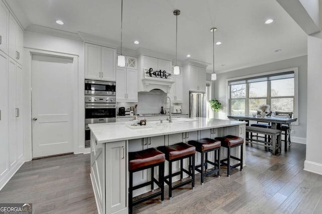 kitchen with appliances with stainless steel finishes, a breakfast bar, a kitchen island with sink, decorative light fixtures, and white cabinetry