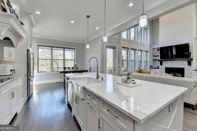 kitchen with stainless steel fridge, sink, pendant lighting, a center island with sink, and white cabinets