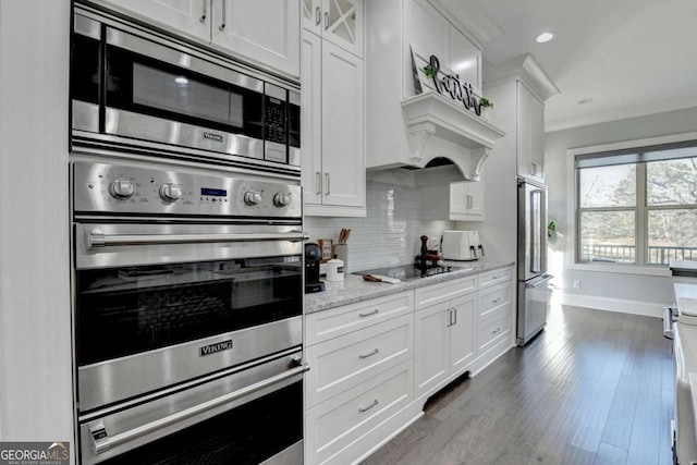 kitchen with appliances with stainless steel finishes, dark hardwood / wood-style flooring, light stone counters, crown molding, and white cabinets