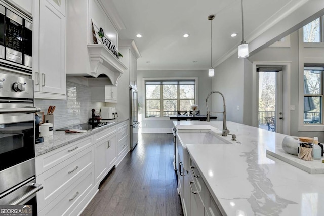 kitchen with light stone countertops, decorative light fixtures, white cabinetry, and stainless steel appliances