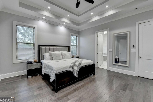 bedroom featuring crown molding, ensuite bath, hardwood / wood-style flooring, ceiling fan, and a tray ceiling