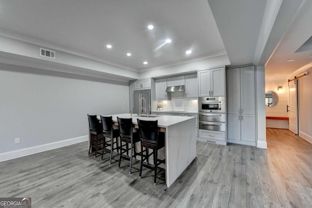 kitchen with a kitchen island with sink, crown molding, gray cabinets, appliances with stainless steel finishes, and a breakfast bar area