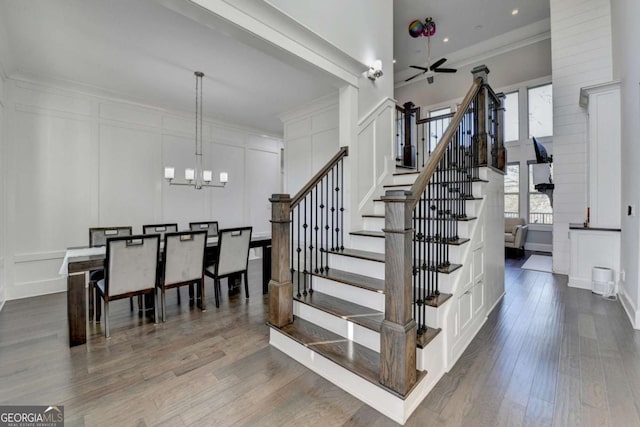 stairway featuring hardwood / wood-style floors, ceiling fan with notable chandelier, and crown molding