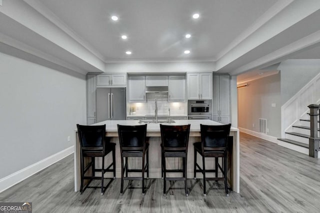 kitchen with light hardwood / wood-style floors, a kitchen bar, a large island with sink, and appliances with stainless steel finishes