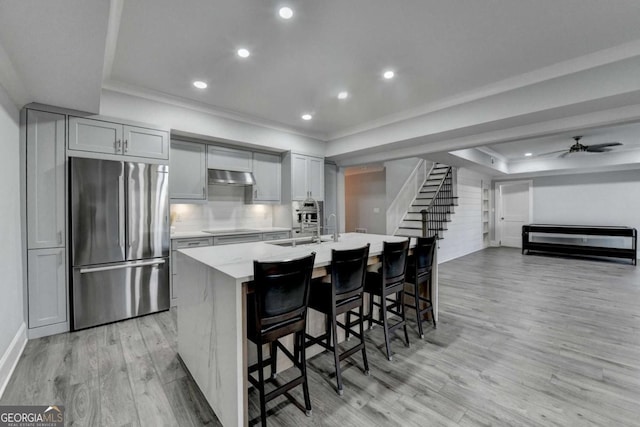 kitchen with stainless steel refrigerator, a kitchen breakfast bar, a raised ceiling, ventilation hood, and an island with sink