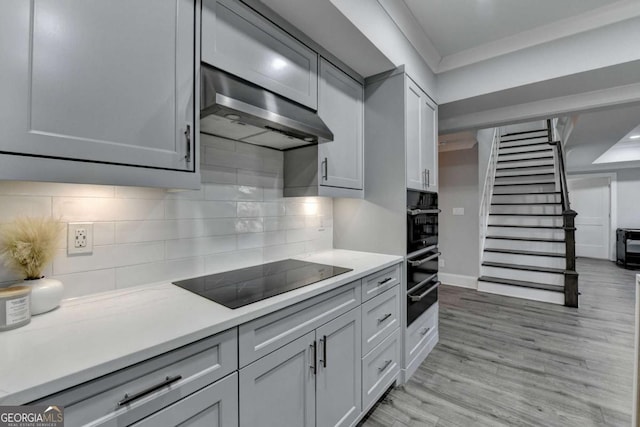 kitchen with gray cabinetry, exhaust hood, black appliances, light hardwood / wood-style flooring, and tasteful backsplash