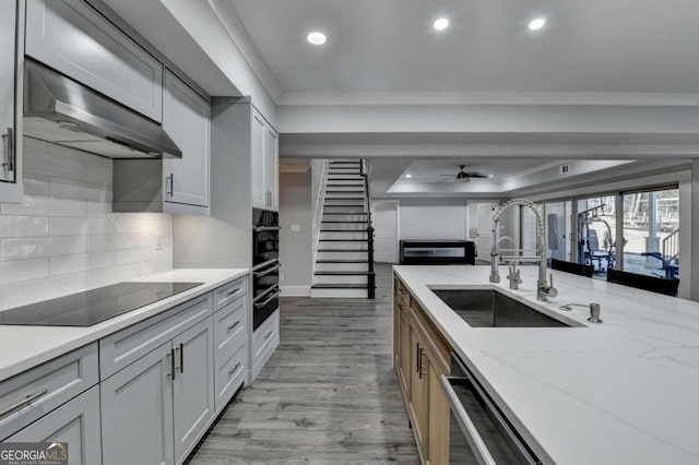 kitchen with ceiling fan, sink, light stone counters, range hood, and black appliances