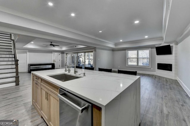 kitchen featuring dishwasher, a raised ceiling, sink, a fireplace, and an island with sink