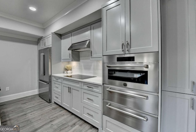 kitchen featuring appliances with stainless steel finishes, light wood-type flooring, tasteful backsplash, crown molding, and exhaust hood