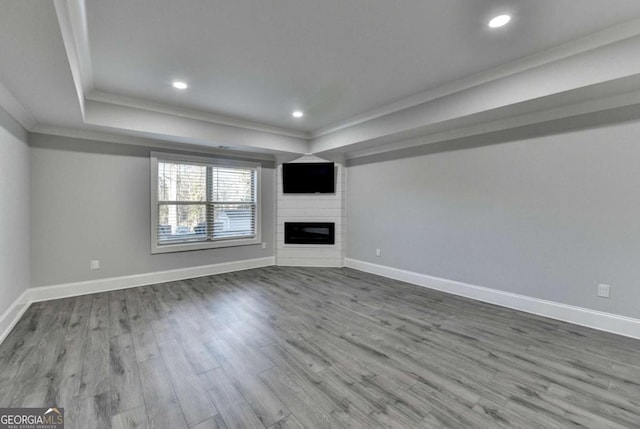 unfurnished living room featuring a fireplace, hardwood / wood-style flooring, a raised ceiling, and crown molding