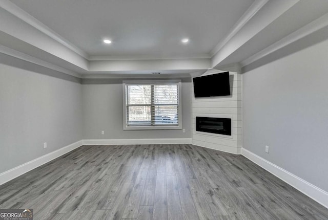 unfurnished living room with a fireplace, hardwood / wood-style flooring, a raised ceiling, and ornamental molding