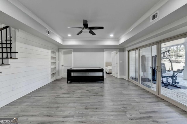 unfurnished bedroom with access to outside, ceiling fan, a tray ceiling, and light wood-type flooring