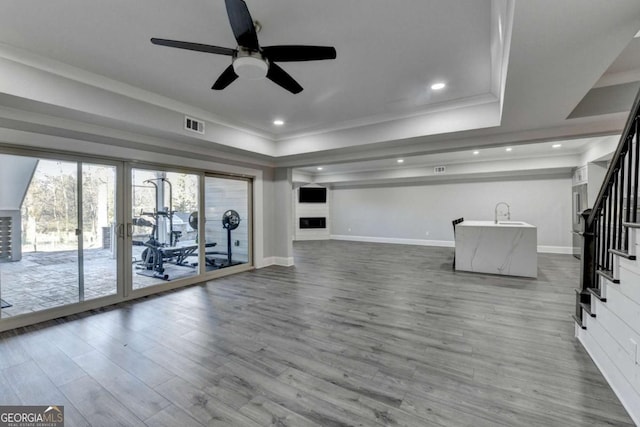 exercise room with ceiling fan, a raised ceiling, wood-type flooring, and crown molding