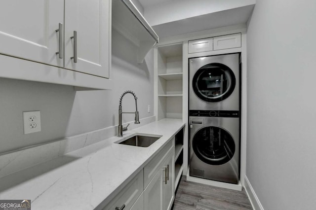 laundry room featuring cabinets, sink, stacked washing maching and dryer, and light hardwood / wood-style flooring