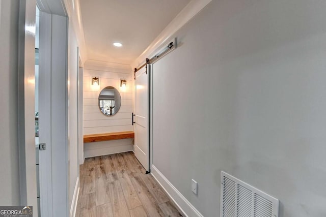 hallway featuring a barn door, ornamental molding, and light wood-type flooring