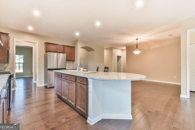 kitchen with a kitchen island with sink, hanging light fixtures, light stone countertops, dark hardwood / wood-style flooring, and stainless steel appliances