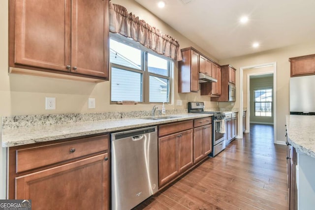 kitchen with hardwood / wood-style floors, appliances with stainless steel finishes, light stone counters, and sink