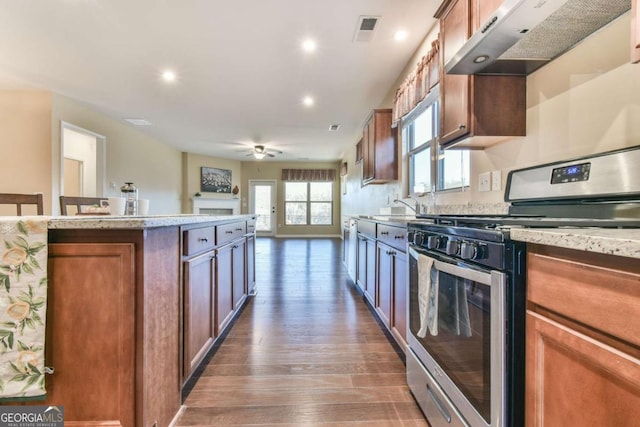 kitchen with light stone counters, stainless steel gas range, extractor fan, ceiling fan, and dark wood-type flooring