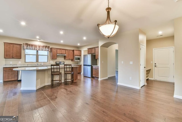 kitchen featuring a kitchen bar, stainless steel appliances, hardwood / wood-style flooring, a kitchen island, and hanging light fixtures