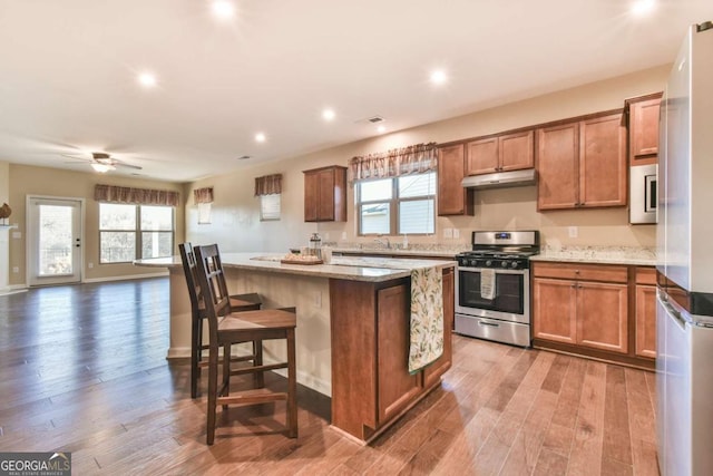 kitchen with hardwood / wood-style floors, a kitchen bar, gas range, a kitchen island, and light stone counters