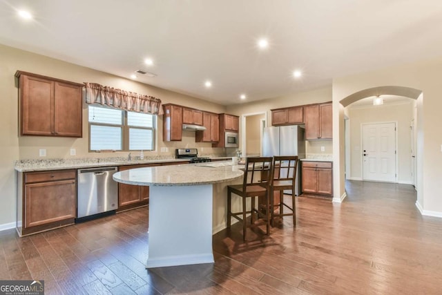 kitchen with a center island, stainless steel appliances, light stone counters, dark hardwood / wood-style floors, and a breakfast bar area