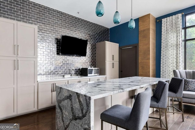 kitchen featuring dark wood-type flooring, sink, white cabinetry, light stone counters, and pendant lighting