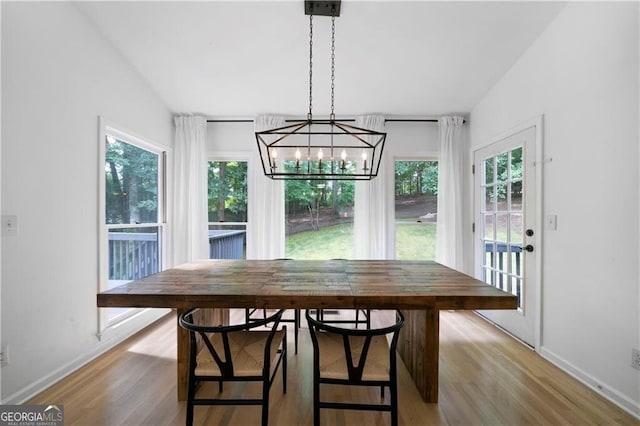 dining area with light hardwood / wood-style floors, vaulted ceiling, and an inviting chandelier