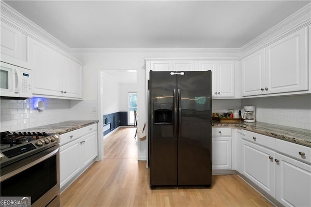 kitchen featuring crown molding, dark stone countertops, gas stove, white cabinetry, and fridge with ice dispenser