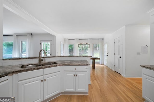 kitchen featuring pendant lighting, light wood-type flooring, white cabinetry, and sink