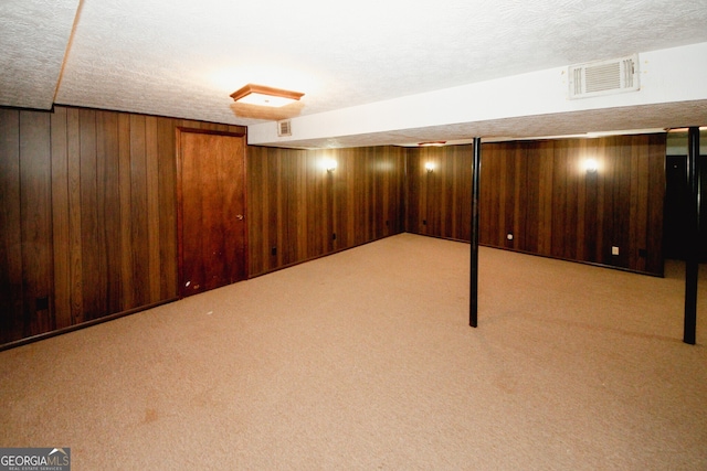 basement featuring a textured ceiling, light carpet, and wood walls