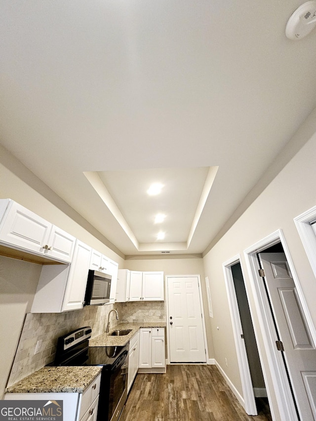 kitchen with electric range oven, sink, a tray ceiling, white cabinetry, and light stone counters