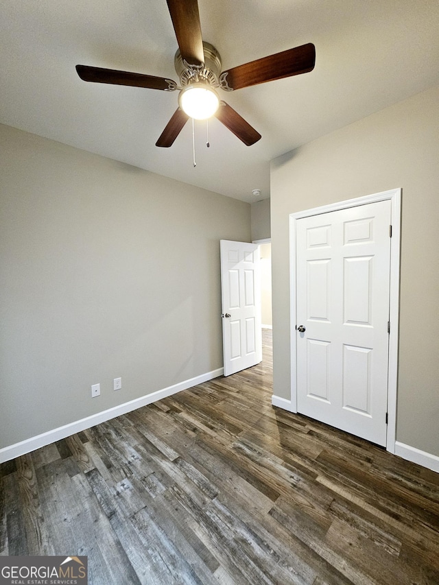 unfurnished bedroom with ceiling fan, a closet, and dark wood-type flooring