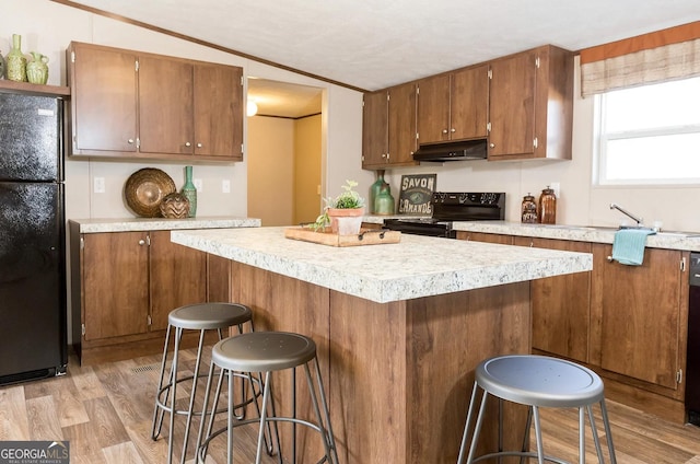 kitchen with crown molding, light wood-type flooring, a breakfast bar area, and black appliances