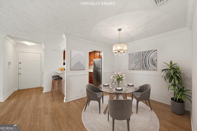 dining space featuring a textured ceiling, light wood-type flooring, crown molding, and an inviting chandelier