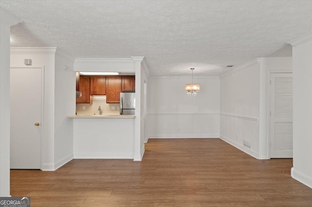 kitchen featuring decorative backsplash, ornamental molding, pendant lighting, light hardwood / wood-style flooring, and stainless steel refrigerator