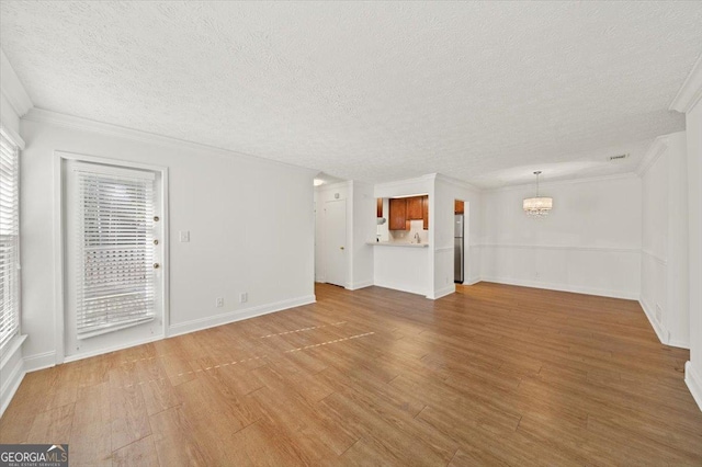 unfurnished living room with crown molding, light hardwood / wood-style flooring, a chandelier, and a textured ceiling