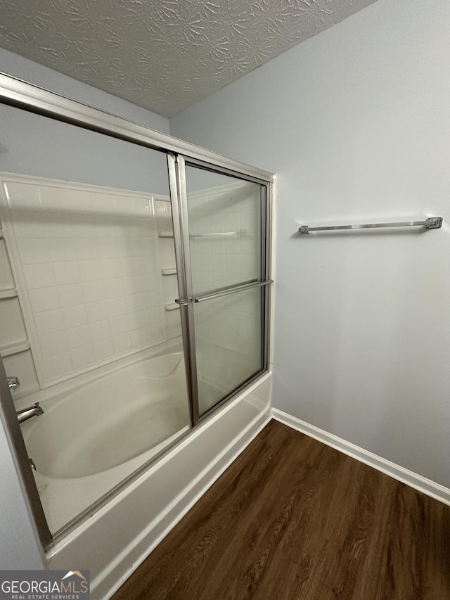 bathroom featuring enclosed tub / shower combo, wood-type flooring, and a textured ceiling