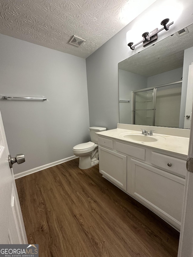 bathroom featuring walk in shower, vanity, a textured ceiling, wood-type flooring, and toilet