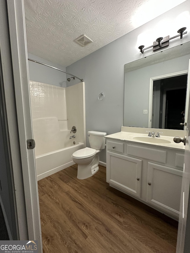 full bathroom with vanity, shower / washtub combination, hardwood / wood-style flooring, toilet, and a textured ceiling